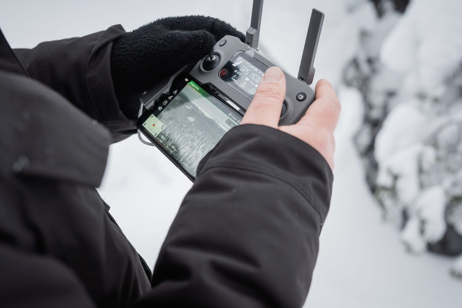 Gloved hands working a drone controller with a map on its screen, in snow.