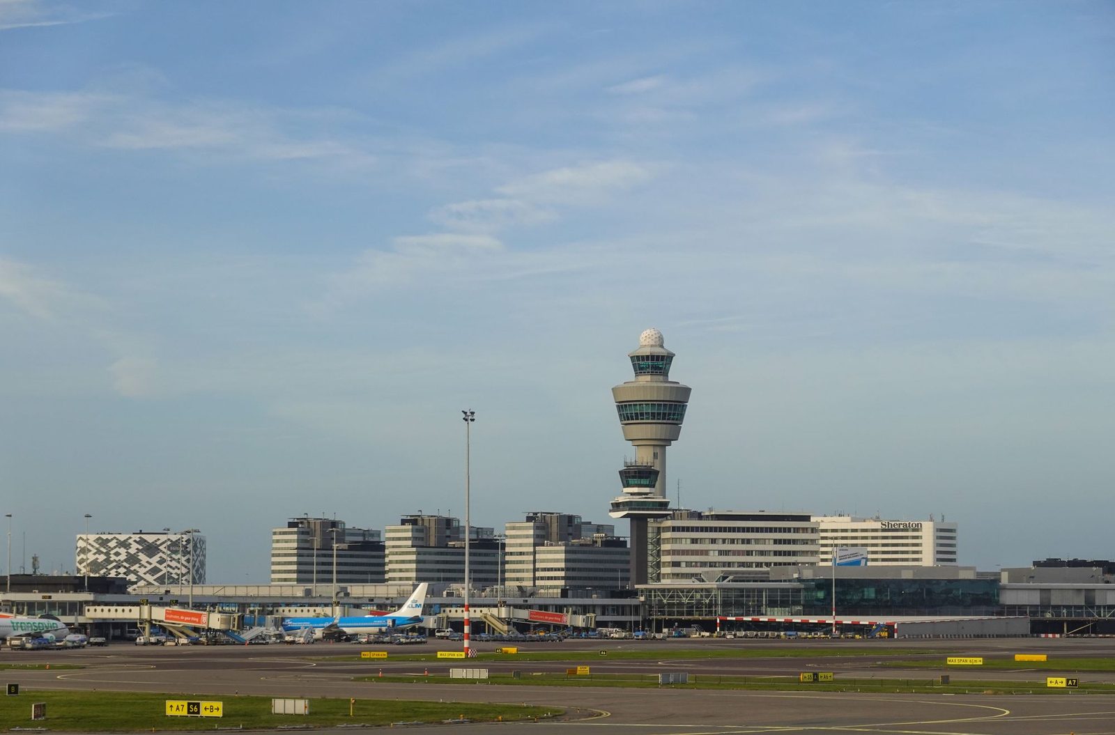 A wide view across an airport apron with the control tower rising behind the terminal.