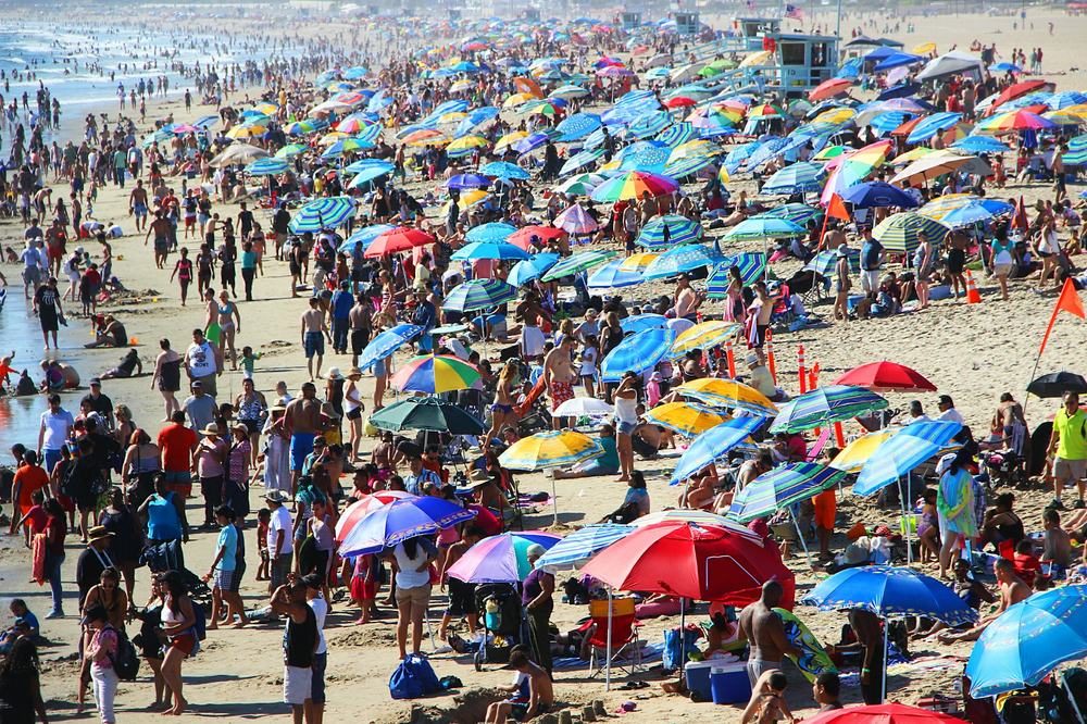 An aerial view of a packed beach, the sand covered with hundreds of parasols and people.