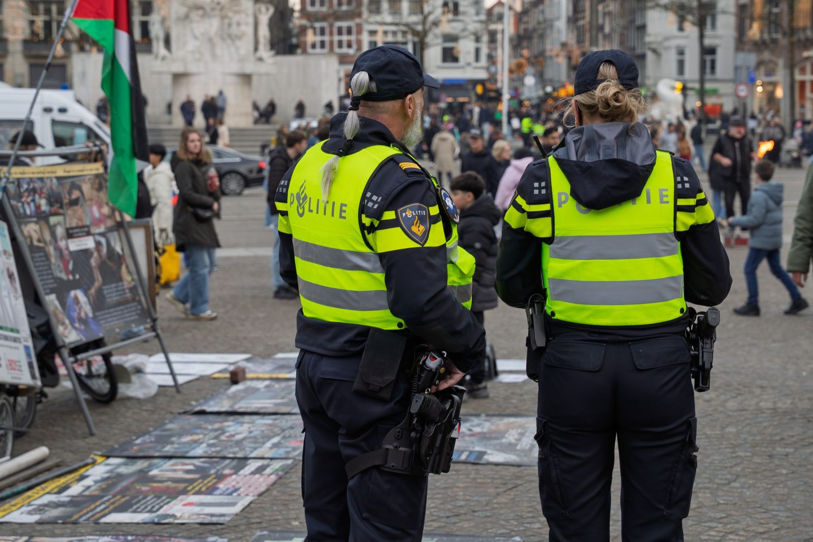 Two police officers in high-visibility jackets watching a busy city square.