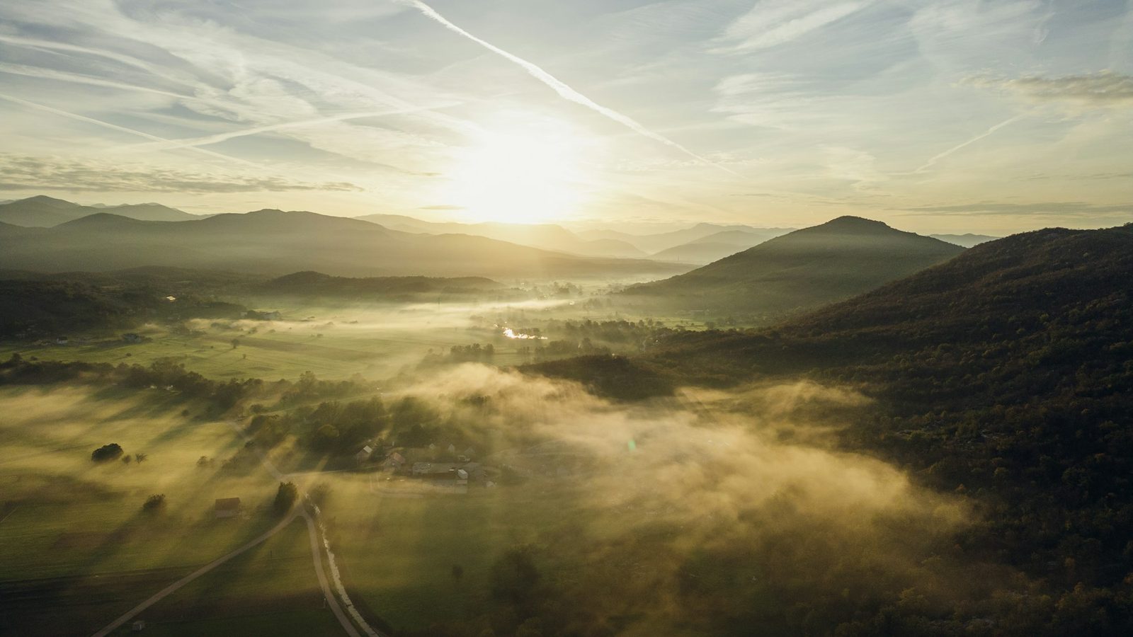 Low sunlight raking across mist-filled valleys and wooded ridges, seen from the air.