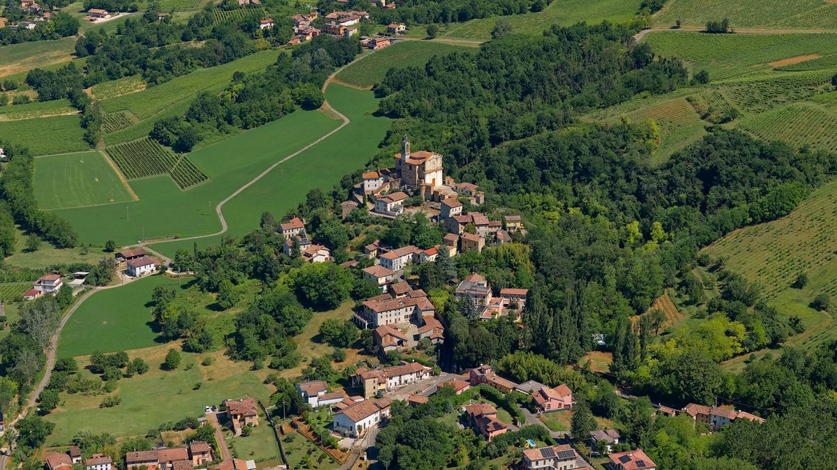 An aerial view of a village with a church tower, surrounded by fields and woodland.