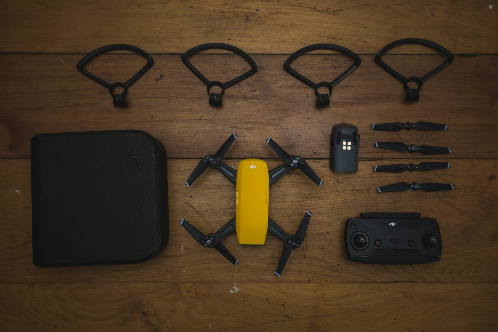 A yellow folding drone laid out with its controller, spare propellers, prop guards and case.