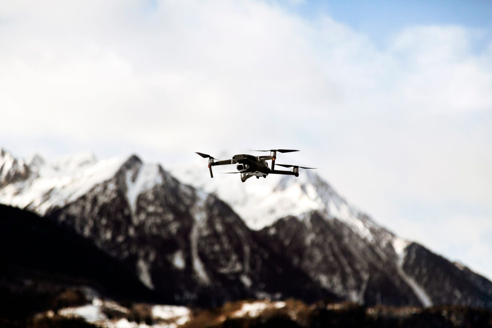 A camera drone hovering in front of snow-covered mountain peaks.