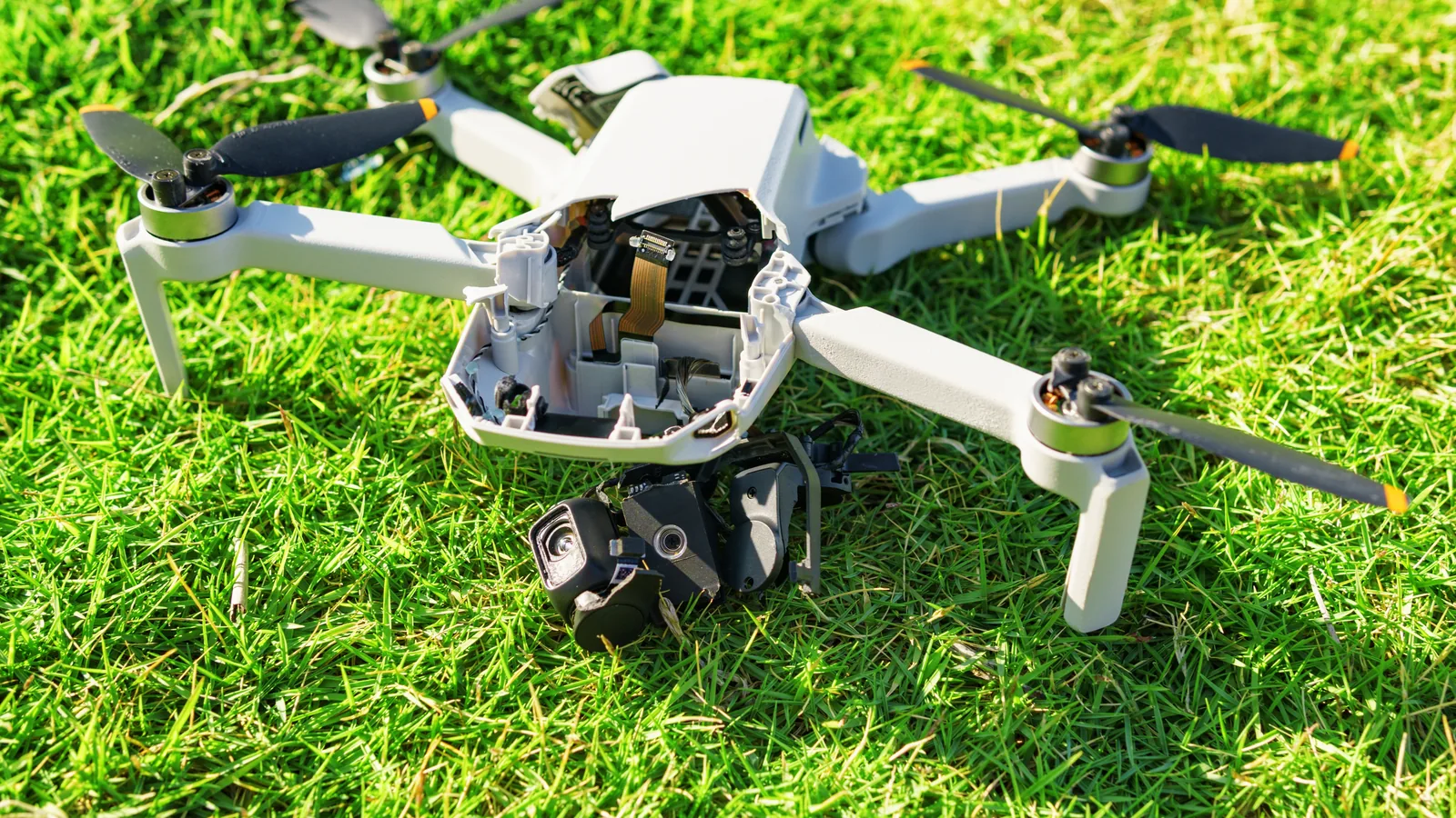 Camera drone with a broken body and detached gimbal after a crash on grass.