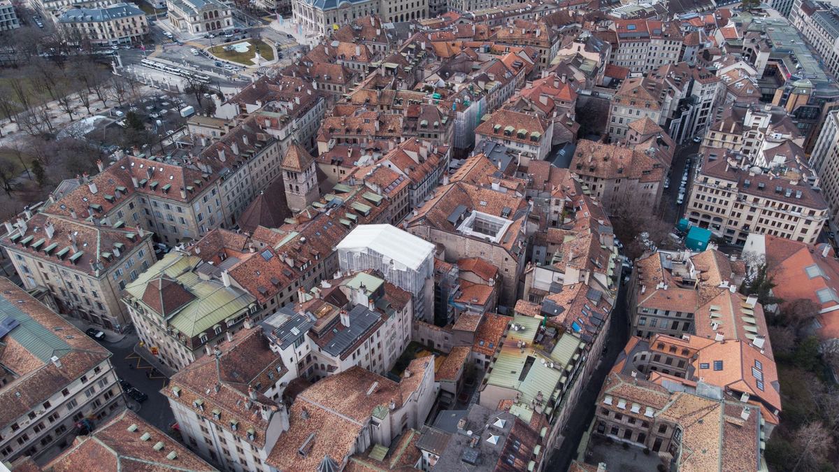 A steep aerial view over the packed tiled roofs and courtyards of an old town.