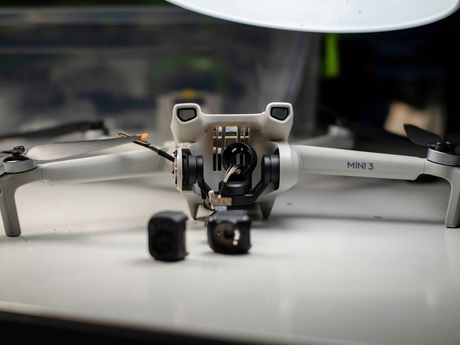 A small camera drone partly disassembled on a bench, with its gimbal and loose parts exposed.