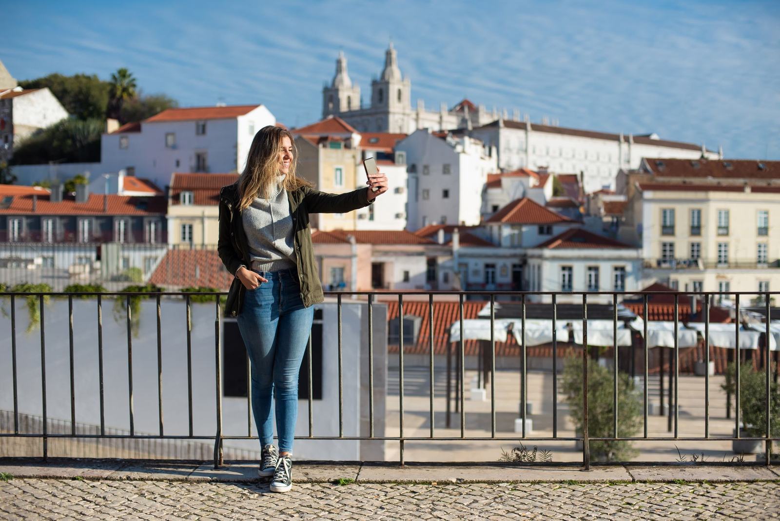 A traveller photographing herself at a railing above a city of tiled roofs.