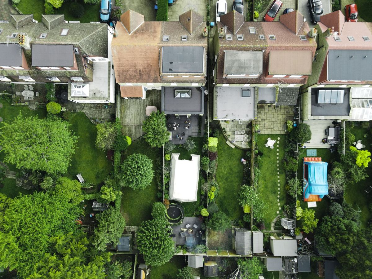 A straight-down aerial view of back gardens, patios and a swimming pool behind a row of houses.
