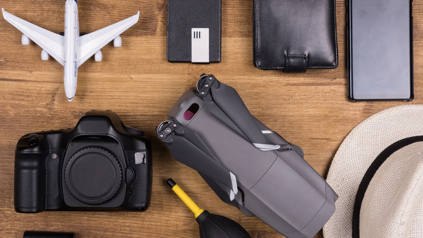 Folded camera drone, phone, wallet, camera and travel accessories arranged beside a model aircraft.