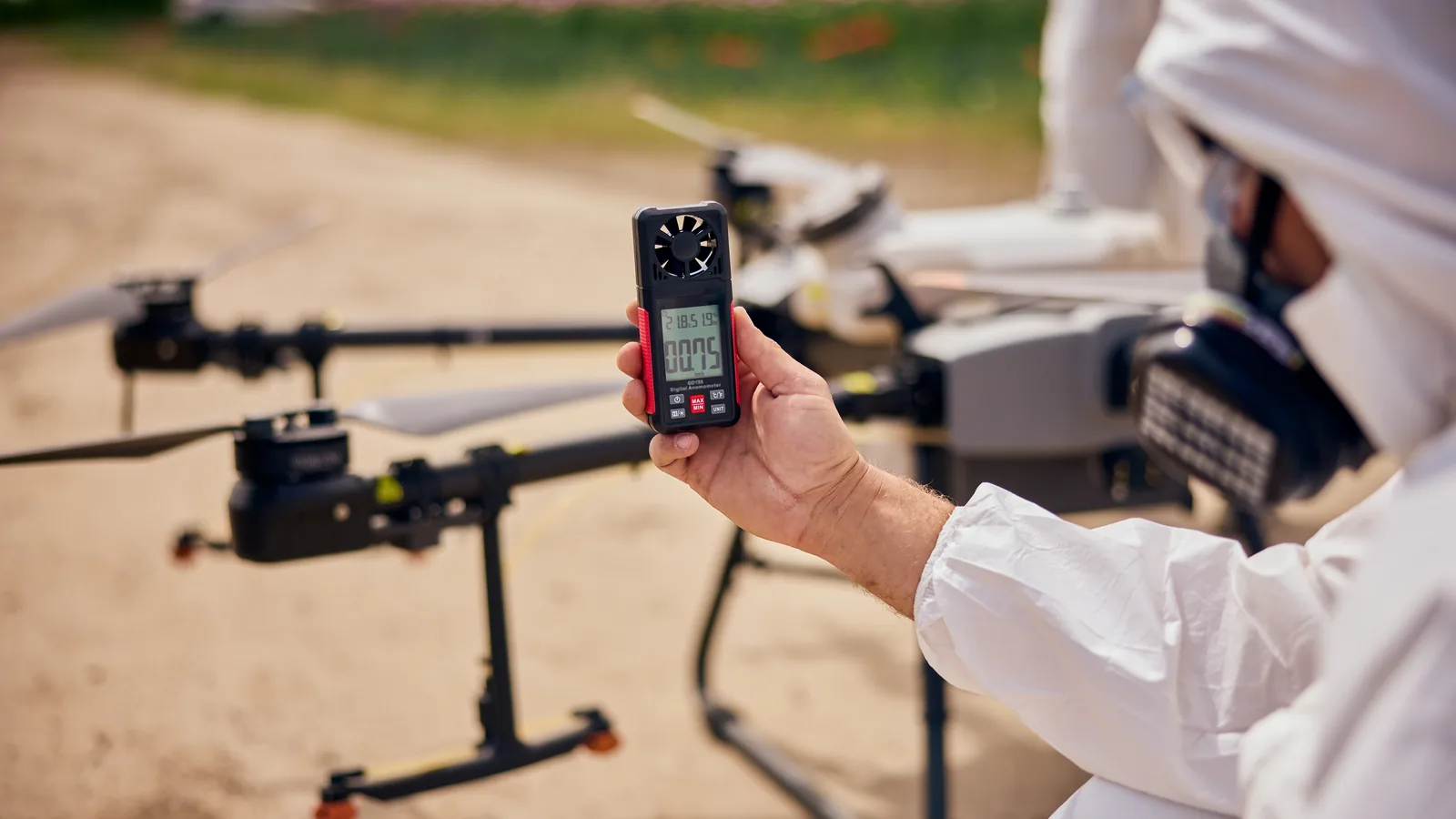 Drone operator measuring wind speed with a handheld anemometer before take-off.