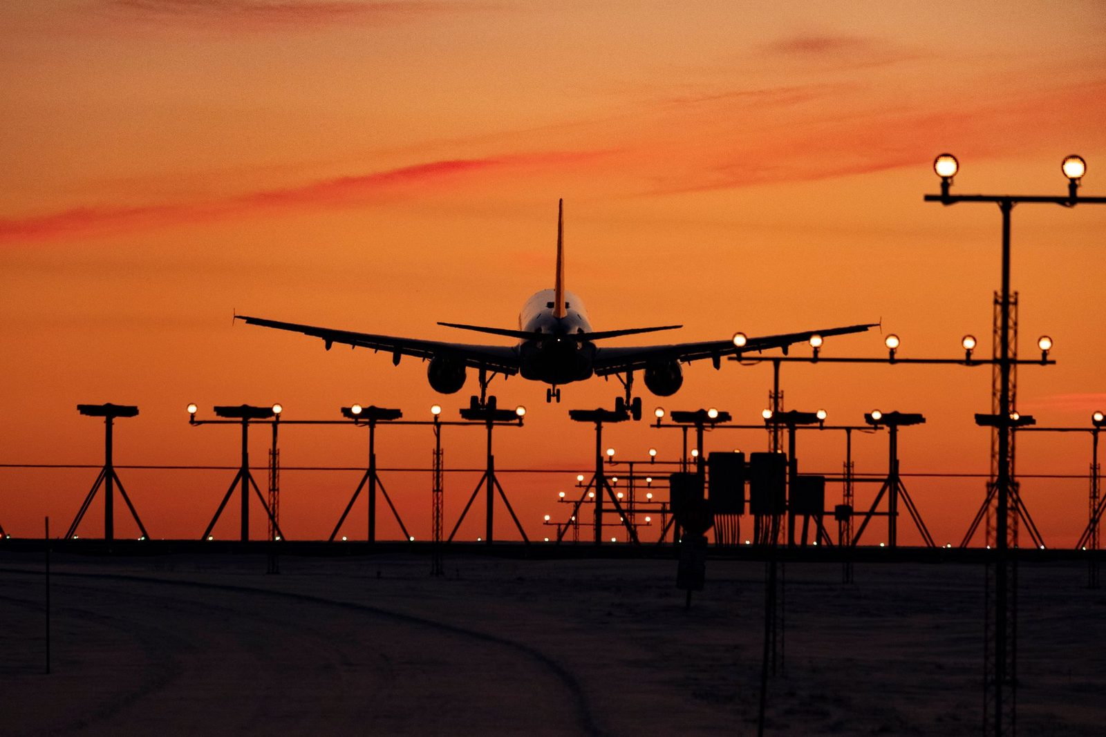 An airliner on final approach at sunset, seen head-on above a line of approach lights.
