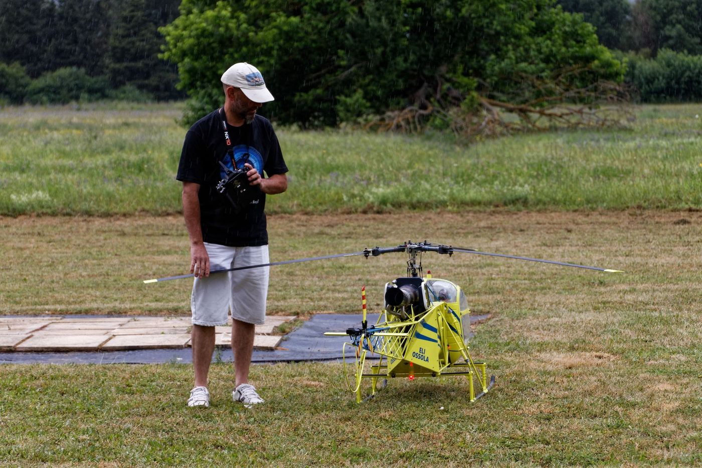 A man on a grass field holding a transmitter, flying a large radio-controlled model helicopter.