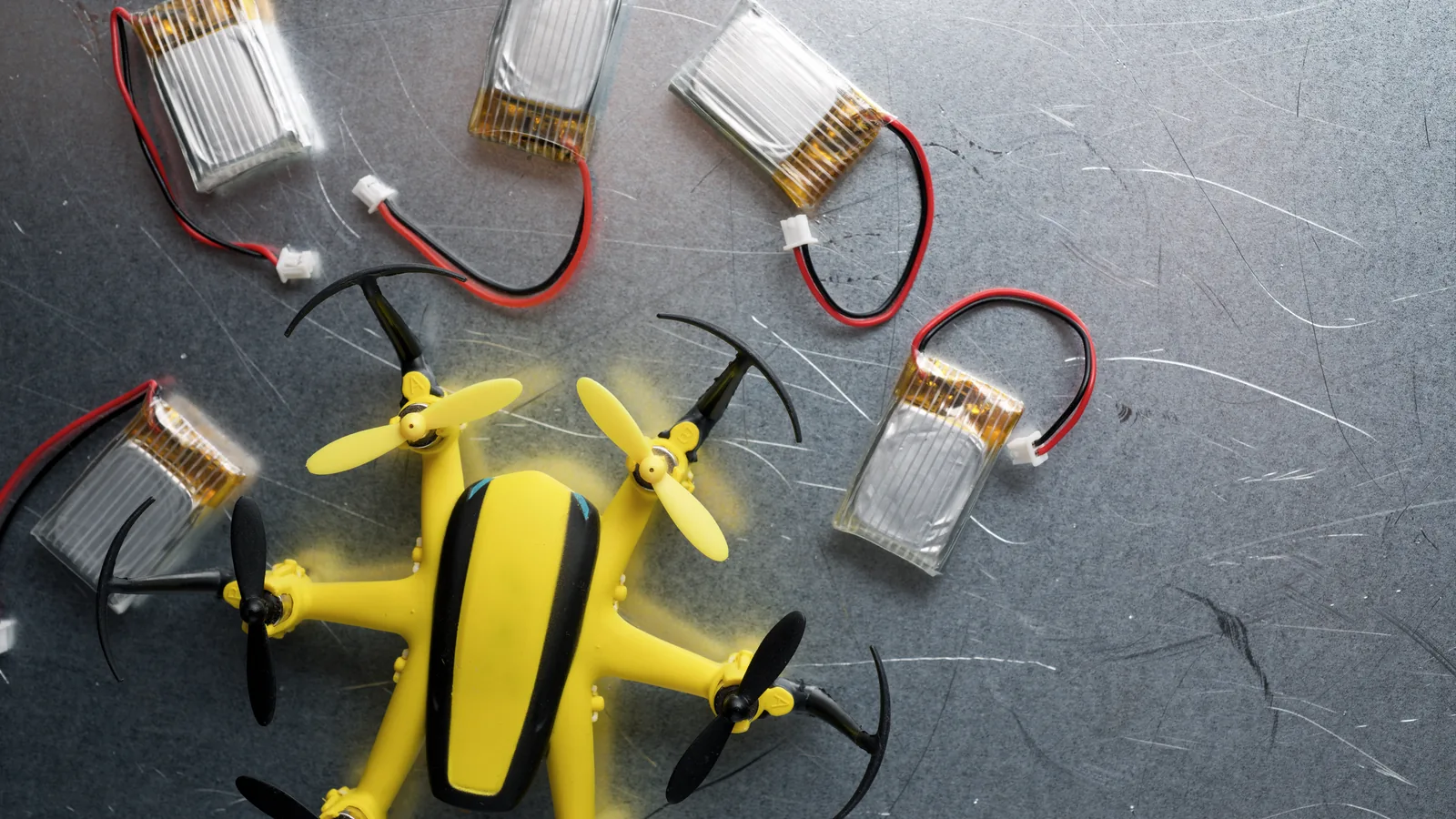 Loose lithium-polymer drone batteries with exposed leads beside a small quadcopter.