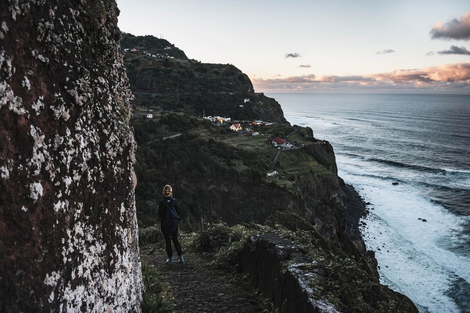 A hiker on a dramatic coastal trail above the Atlantic Ocean in Madeira, Portugal.