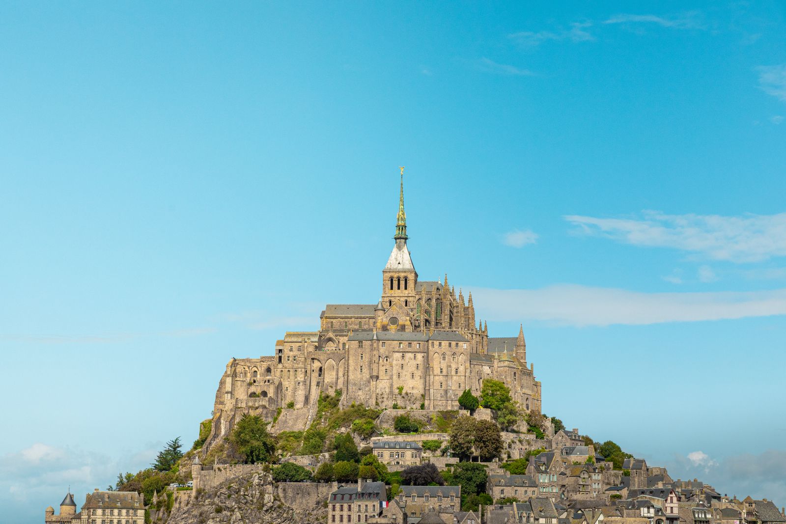 Mont-Saint-Michel abbey and village rising above the Normandy landscape under a blue sky.