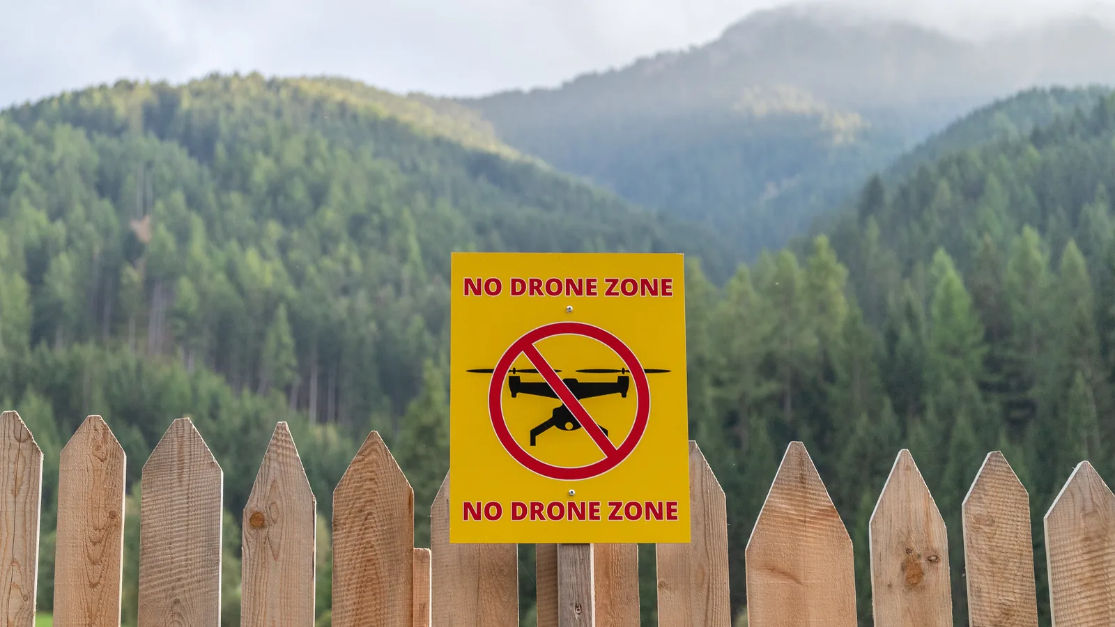 No-drone-zone sign on a fence in a mountain landscape.