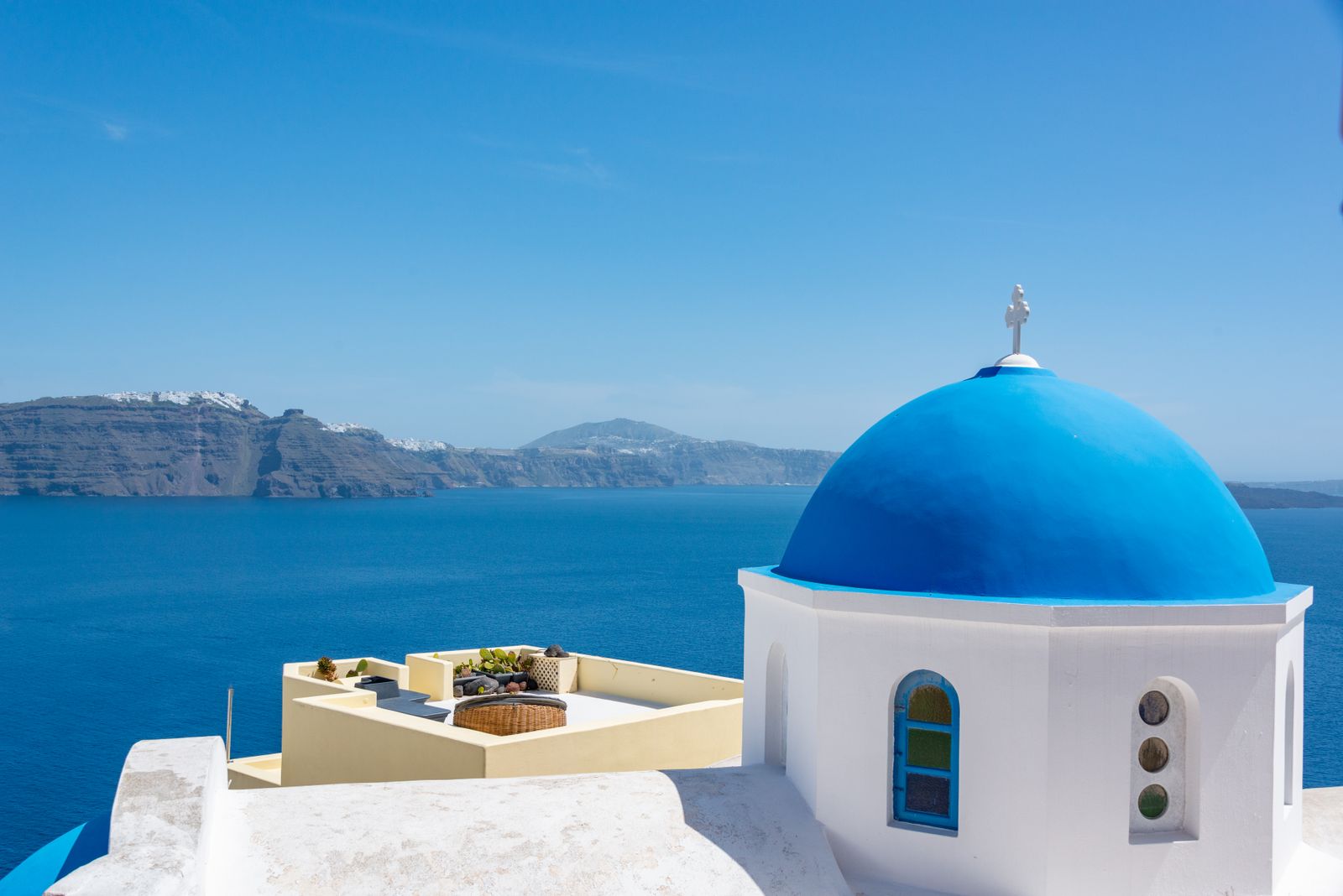 A blue-domed white church overlooking the caldera and Aegean Sea in Santorini, Greece.