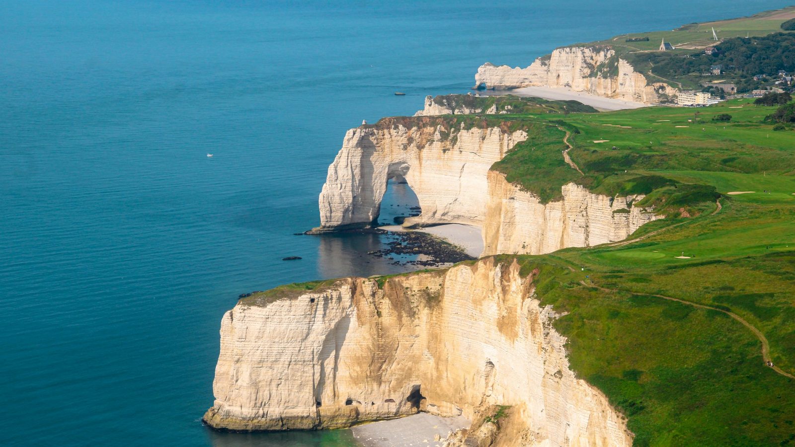 An aerial view of white chalk cliffs and a natural sea arch above green clifftop fields.