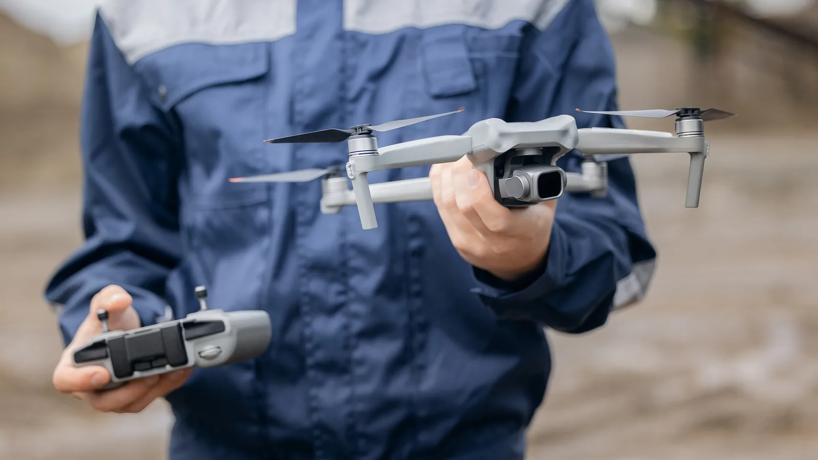 Remote pilot holding a camera drone and controller while preparing to fly