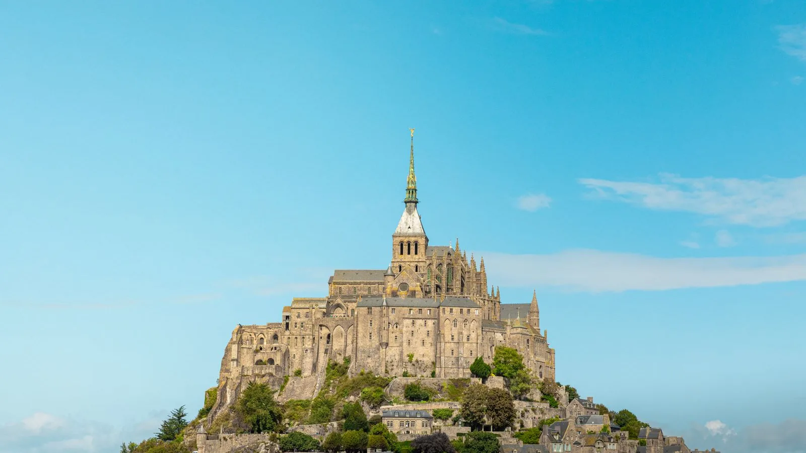 Mont-Saint-Michel abbey and village rising above the Normandy landscape under a blue sky.
