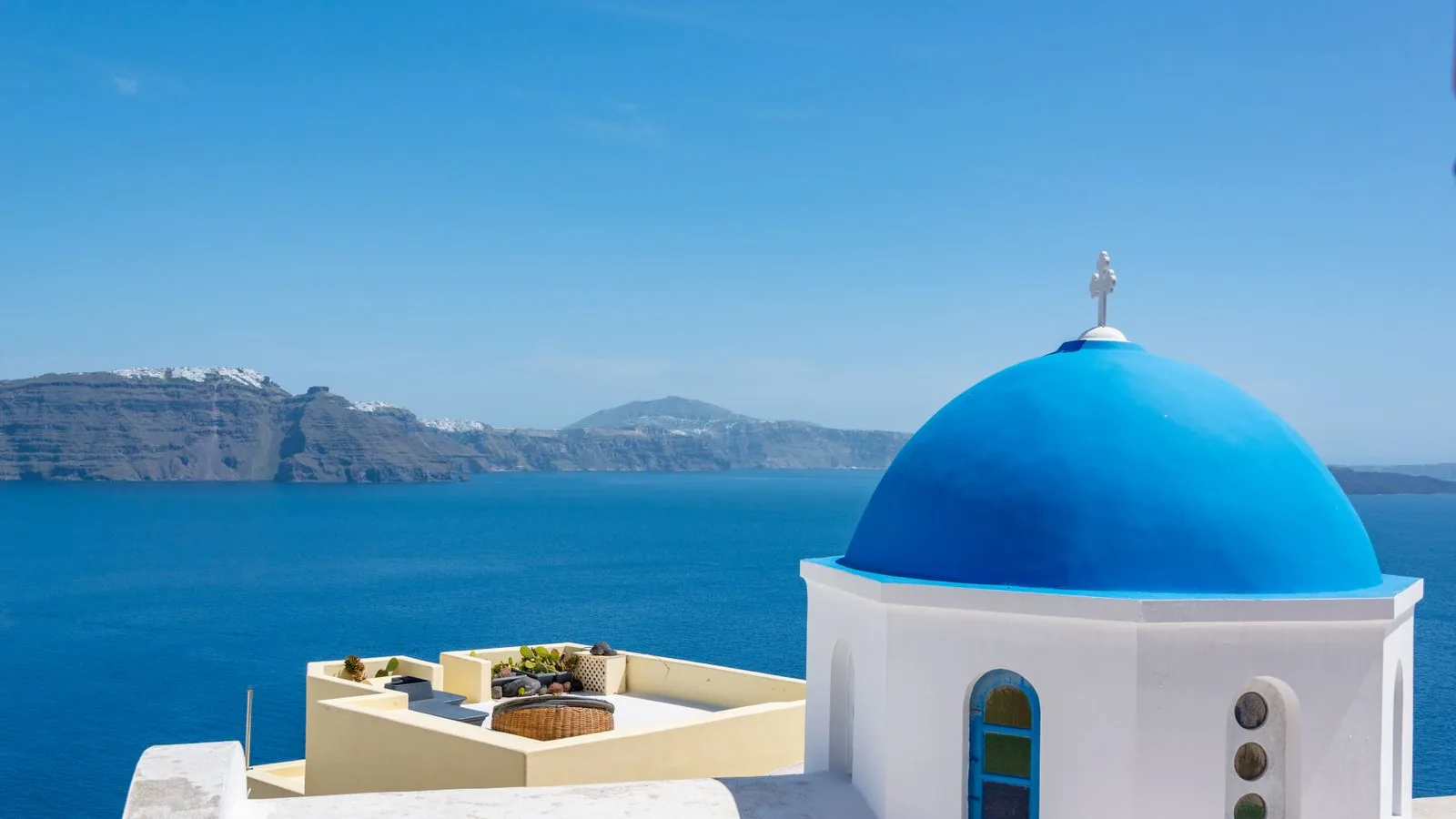 A blue-domed white church overlooking the caldera and Aegean Sea in Santorini, Greece.