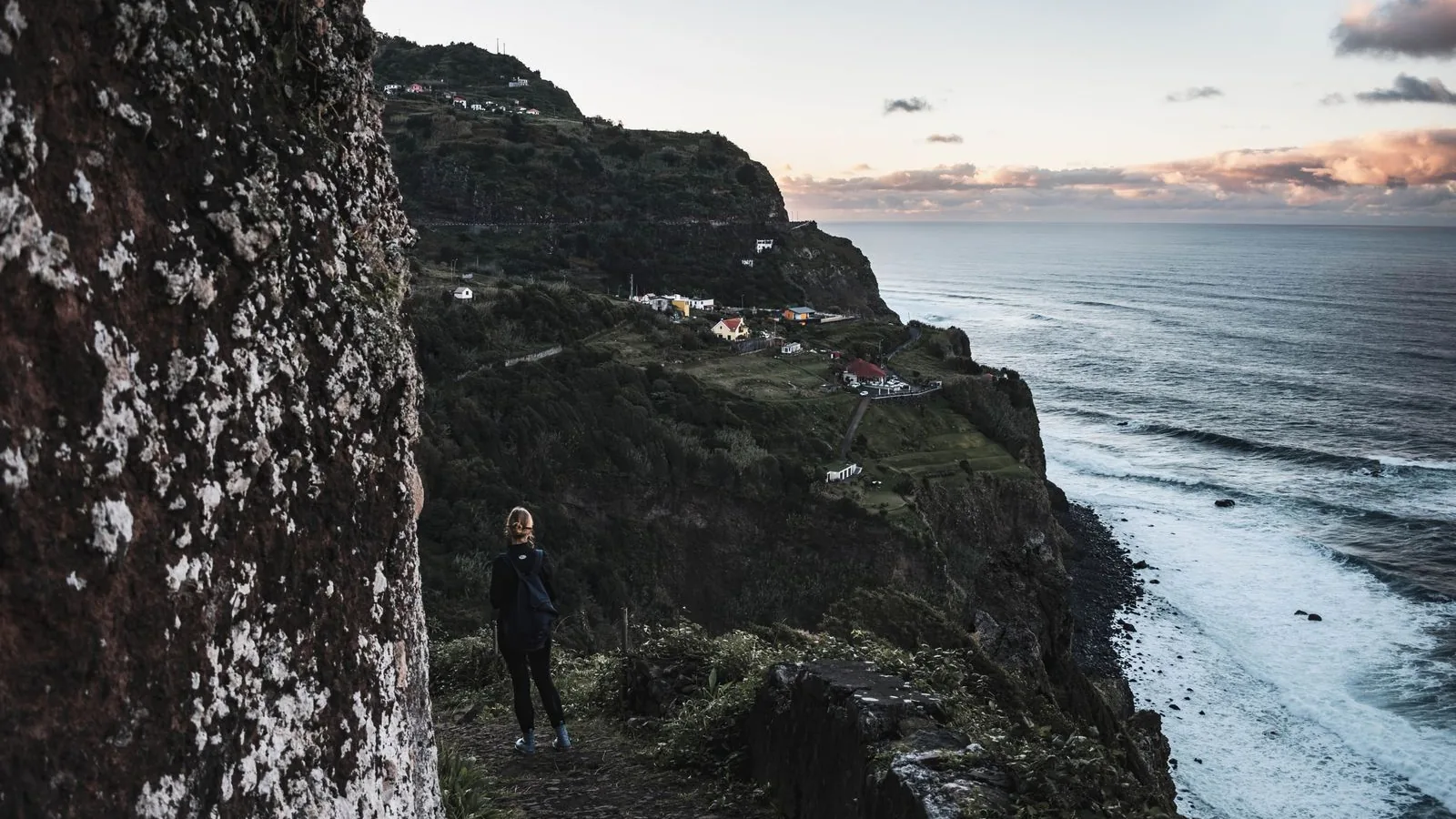 A hiker on a dramatic coastal trail above the Atlantic Ocean in Madeira, Portugal.